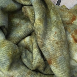 May include: A green and brown fabric with a tie-dye pattern. The fabric has a textured surface and is folded in a pile.