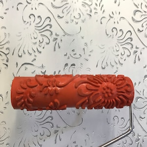 May include: Orange paint roller with a floral design. The roller is attached to a metal handle.