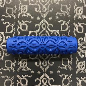 May include: Blue paint roller with a decorative pattern. The pattern is a repeating design of swirls and loops.