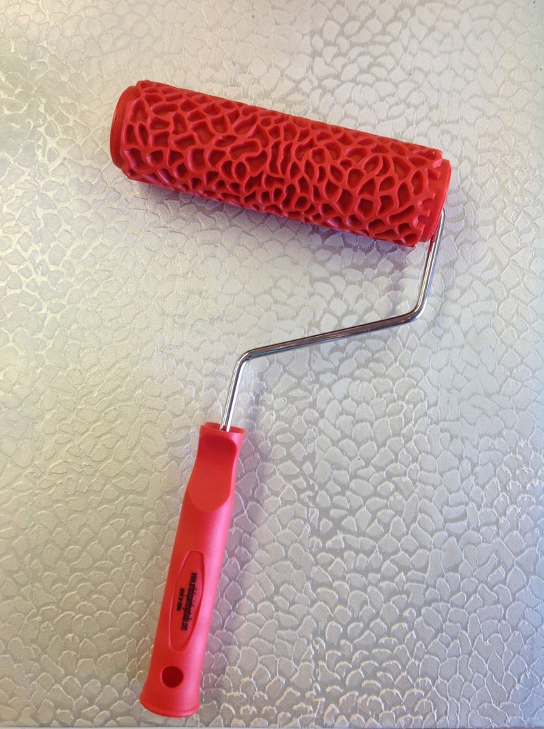 May include: Red paint roller with a textured pattern and a silver handle. The roller is designed to create a textured finish on walls or other surfaces.