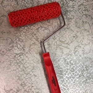 May include: Red paint roller with a textured, honeycomb-like pattern. The roller is attached to a silver metal handle with a red plastic grip. The handle has the text "Made in China" printed on it.