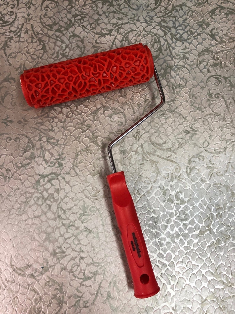 May include: Red paint roller with a textured, honeycomb-like pattern. The roller is attached to a silver metal handle with a red plastic grip. The handle has the text "Made in China" printed on it.