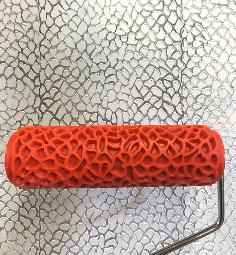 May include: A red paint roller with a textured pattern of small, irregular shapes. The roller is designed to create a decorative, textured finish on walls or other surfaces.