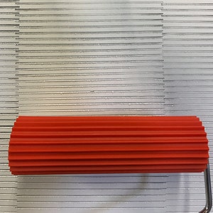 May include: A red rubber roller with a ribbed surface. The roller is used for smoothing out grout or adhesive.