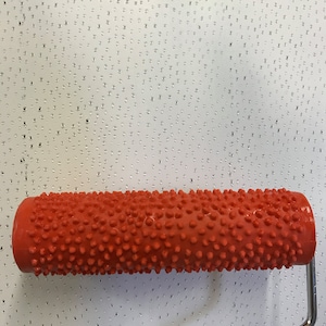 May include: A red textured paint roller with a metal handle. The roller is designed to create a textured finish on walls.