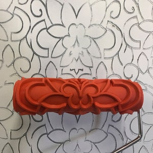 May include: A red rubber paint roller with a decorative floral pattern. The roller is designed to create a textured effect on walls.