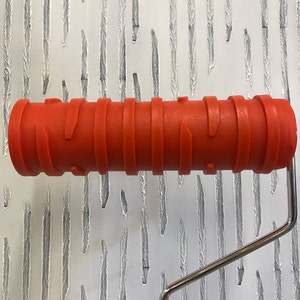 May include: A red textured paint roller with a silver handle. The roller is designed to create a vertical, linear pattern on walls.
