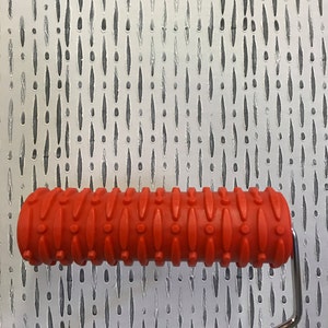 May include: A red textured paint roller with a metal handle. The roller is designed to create a pattern of small circles and lines on a wall.