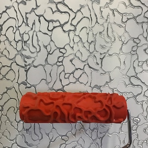 May include: Red paint roller with a textured pattern of irregular shapes. The roller is designed to create a unique, organic look on walls.