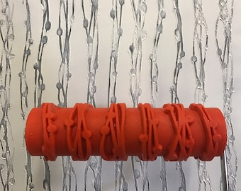 May include: A red rubber roller with a repeating pattern of vines and berries. The roller is attached to a metal handle.