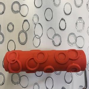 May include: A red paint roller with a pattern of overlapping circles. The roller is designed to create a textured, circular pattern on walls.