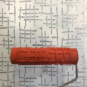 May include: A red paint roller with a textured pattern of criss-crossed lines. The roller is being used to create a similar pattern on a white wall.