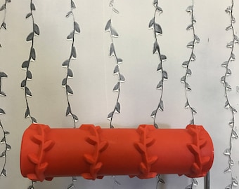May include: A red paint roller with a leaf pattern design. The roller is being used to create a repeating pattern on a white wall.