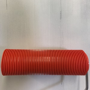May include: A red textured paint roller with a metal handle. The roller is designed to create a textured finish on walls or other surfaces.