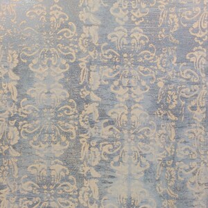 May include: A close-up of a textured surface with a light blue background and a beige pattern of repeating floral designs.