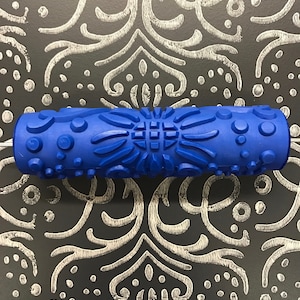 May include: Blue paint roller with a textured design. The roller has a variety of patterns including circles, squares, and swirls.