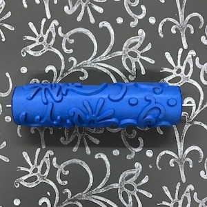 May include: A blue paint roller with a decorative pattern of swirls and flowers. The roller is designed to create a unique textured effect on walls.