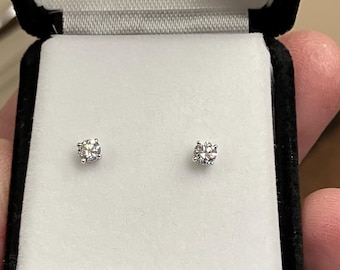 Puede incluir: Un par de pendientes de diamantes presentados en una caja de joyería de terciopelo negro con un interior de satén blanco. Los pendientes son redondos y de aspecto claro y brillante.