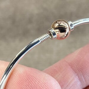 Op de afbeelding: Een zilveren armband met een ros&eacute;gouden bal die erop en eraf geschroefd kan worden.