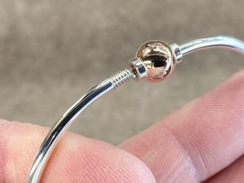 Op de afbeelding: Een zilveren armband met een ros&eacute;gouden bal die erop en eraf geschroefd kan worden.