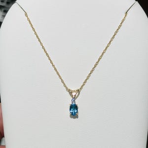 May include: A gold chain necklace with a pendant featuring a blue gemstone surrounded by smaller white gemstones.