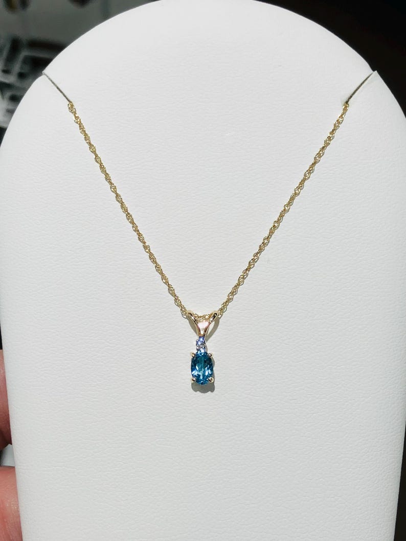 May include: A gold chain necklace with a pendant featuring a blue gemstone surrounded by smaller white gemstones.