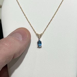 May include: A gold chain necklace with a pendant featuring a blue oval gemstone and a smaller diamond accent.
