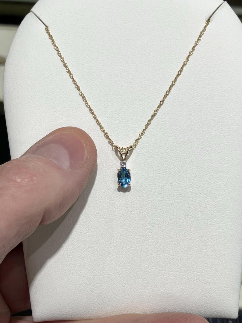 May include: A gold chain necklace with a pendant featuring a blue oval gemstone and a smaller diamond accent.