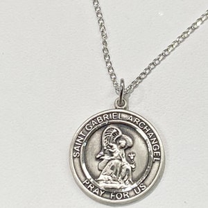 Può includere: Collana con ciondolo in argento con una medaglia rotonda con l'immagine di San Gabriele Arcangelo. La medaglia ha l'iscrizione "San Gabriele Arcangelo prega per noi".