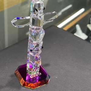 May include: A crystal totem pole figurine with a purple and orange base. The totem pole is made of clear crystal and features a variety of animal figures.