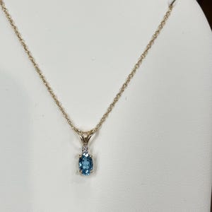 May include: A gold chain necklace with a pendant featuring a blue oval gemstone surrounded by smaller diamonds.