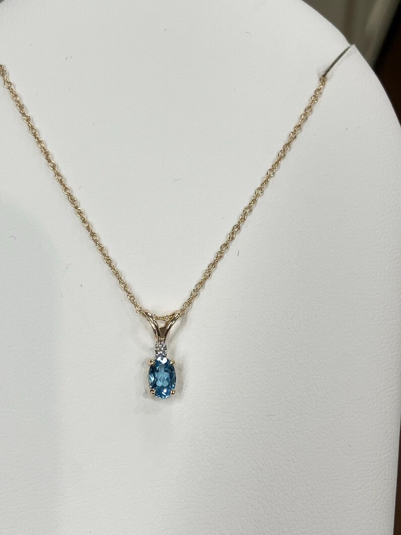 May include: A gold chain necklace with a pendant featuring a blue oval gemstone surrounded by smaller diamonds.