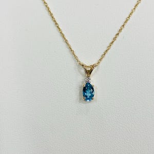 May include: A gold chain necklace with a pendant featuring a blue oval gemstone and a small diamond accent.