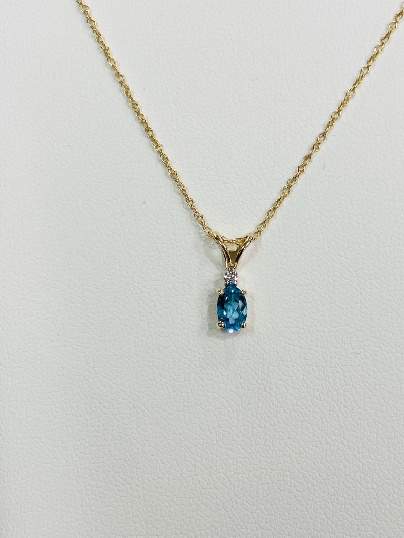 May include: A gold chain necklace with a pendant featuring a blue oval gemstone and a small diamond accent.