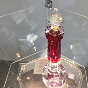 May include: A red crystal lighthouse figurine with a clear glass top. The lighthouse is on a clear glass base.