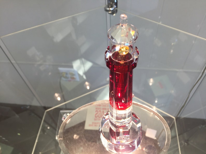 May include: A red crystal lighthouse figurine with a clear glass top. The lighthouse is on a clear glass base.