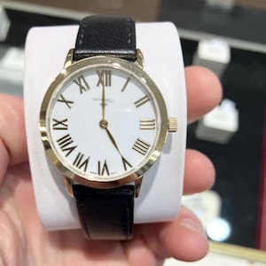 May include: A gold-tone watch with a white face and black leather strap. The watch has Roman numeral hour markers and a gold-tone second hand.