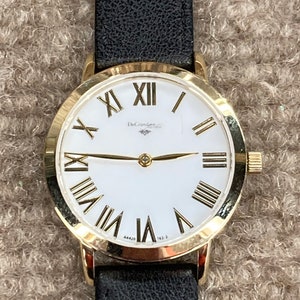May include: A gold-tone wristwatch with a white face and black leather strap. The watch face has Roman numeral hour markers and a DeGramere logo.