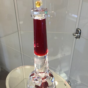 May include: A crystal lighthouse figurine with a red liquid inside and a small gold-colored gemstone at the top.