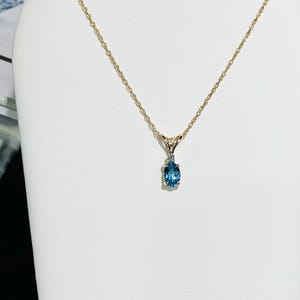 May include: A gold chain necklace with a pendant featuring a blue oval gemstone and a small diamond accent.
