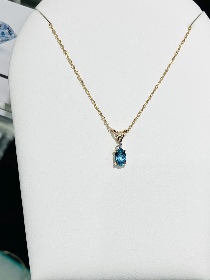 May include: A gold chain necklace with a pendant featuring a blue oval gemstone and a small diamond accent.
