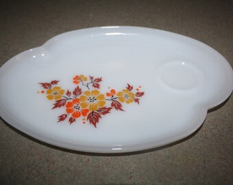 May include: White oval serving tray with a floral design in shades of orange, yellow, and brown. The tray has a small indentation for a cup.