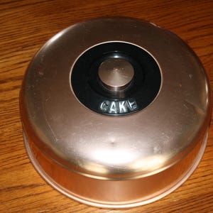 May include: A vintage copper cake dome with a black knob and the word "CAKE" embossed on the top.