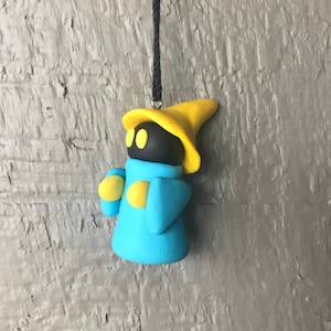 May include: A handmade clay figurine of a wizard in a blue robe and yellow hat. The wizard has a black head with yellow eyes and yellow accents on the arms. The figurine is hanging from a black string.