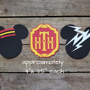 May include: Three paper cutouts on a wood background. The cutouts are approximately 4 inches by 3.5 inches. The cutouts are a black Mickey Mouse head with a red and yellow hat, a red and gold shield with the letters "HTH" in white, and a black Mickey Mouse head with a white lightning bolt.