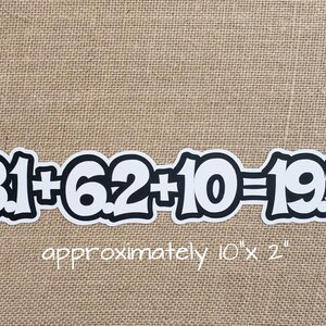 May include: A black and white sticker with the equation "31 + 6.2 + 10 = 19.3" in a bold, rounded font. The sticker is approximately 10 inches long and 2 inches wide. The sticker is on a tan burlap background.