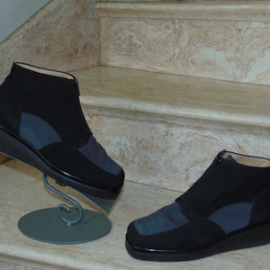 May include: Two pairs of black suede ankle boots with a zipper on the side. The boots have a blue suede panel on the back and a thick black sole.