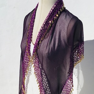 Peut inclure: Un châle en mousseline violet avec des perles dorées et une bordure en crochet. Le châle est drapé sur un mannequin blanc.