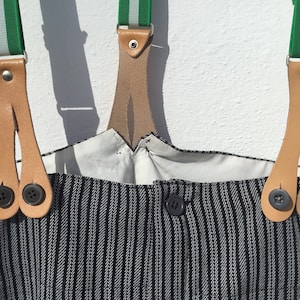 May include: Black and white striped overalls with green and white striped suspenders. The suspenders have leather straps with two buttons on each strap.