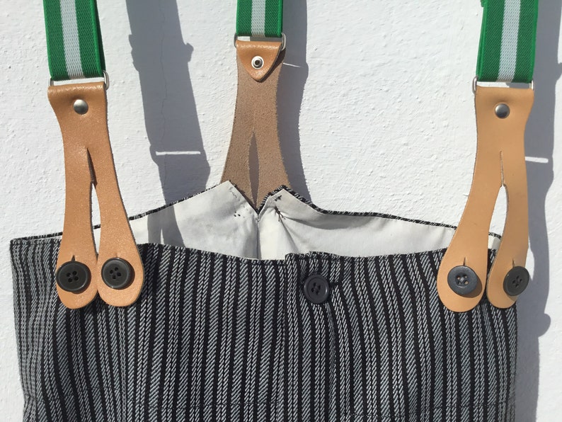 May include: Black and white striped overalls with green and white striped suspenders. The suspenders have leather straps with two buttons on each strap.